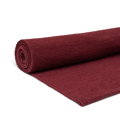 Rolled burgundy cotton yoga mat on a white background.