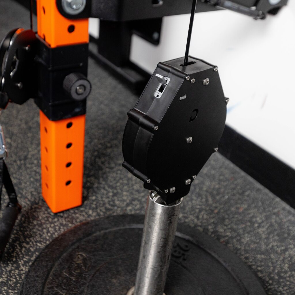 Black metal device with bolts mounted on a steel shaft beside an orange support.
