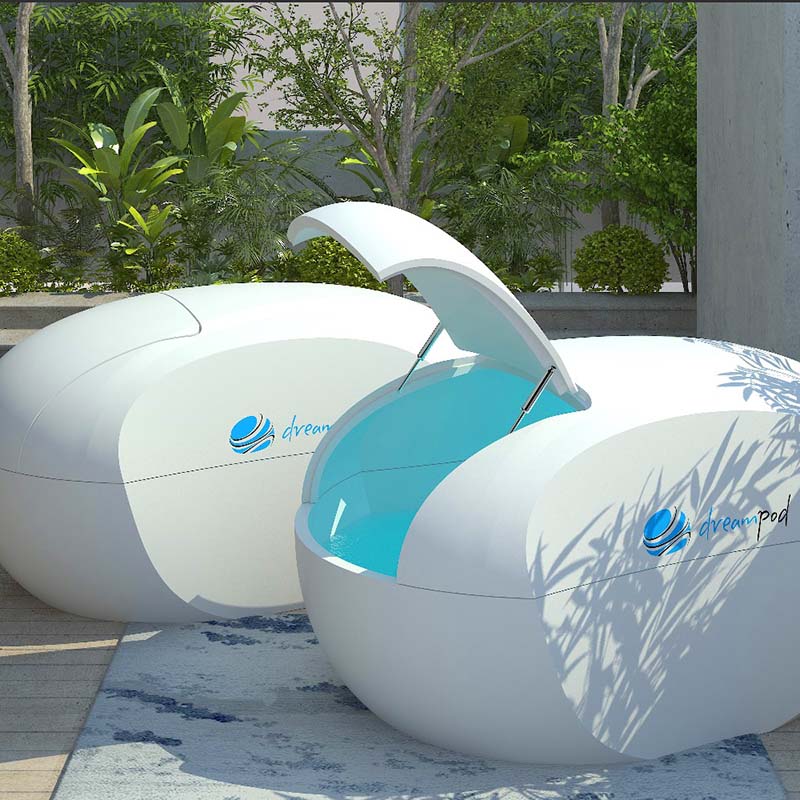 Two Dreampod Home Float Plus sensory isolation pods with open lids, set in a lush garden environment.