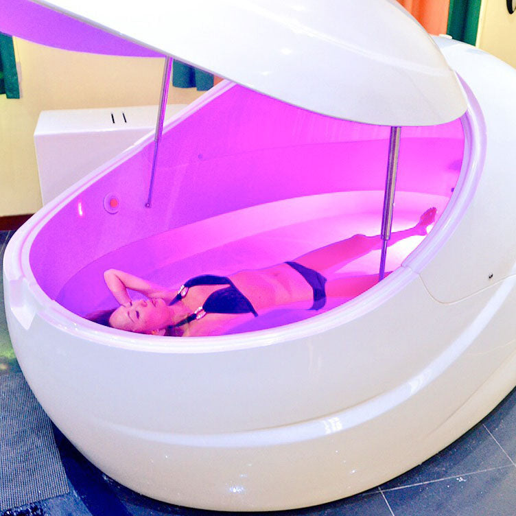 A person relaxing inside a Dreampod V2 Float Pod with soft purple lighting.