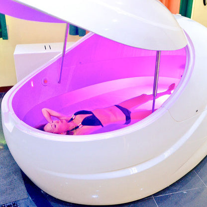A person relaxing inside a Dreampod V2 Float Pod with soft purple lighting.