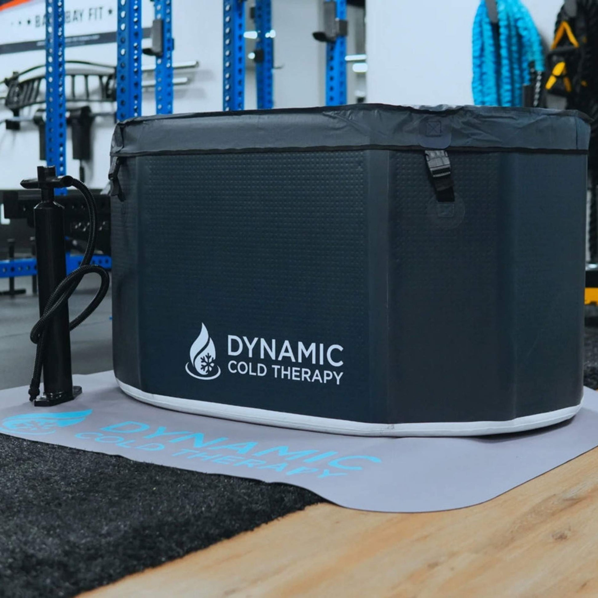 Dynamic Cold Therapy portable ice bath situated on a mat in a gym environment, featuring a black exterior and a pump attached.
