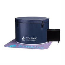 A round, navy blue cold therapy tub with a cover, featuring the logo DYNAMIC COLD THERAPY, positioned next to a black cooling unit on a gray mat with the same logo.