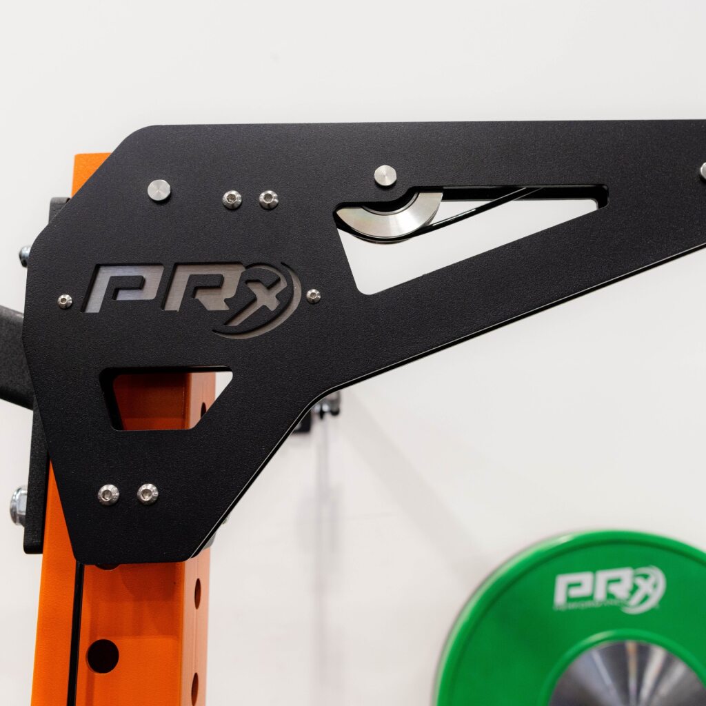 Close-up of a black metal gym machine frame with orange support and a green weight plate.