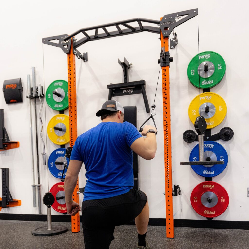 Man in blue shirt using a squat rack in a gym.
