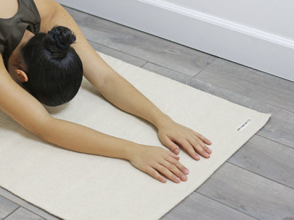Person stretching forward on a light fabric yoga mat indoors.