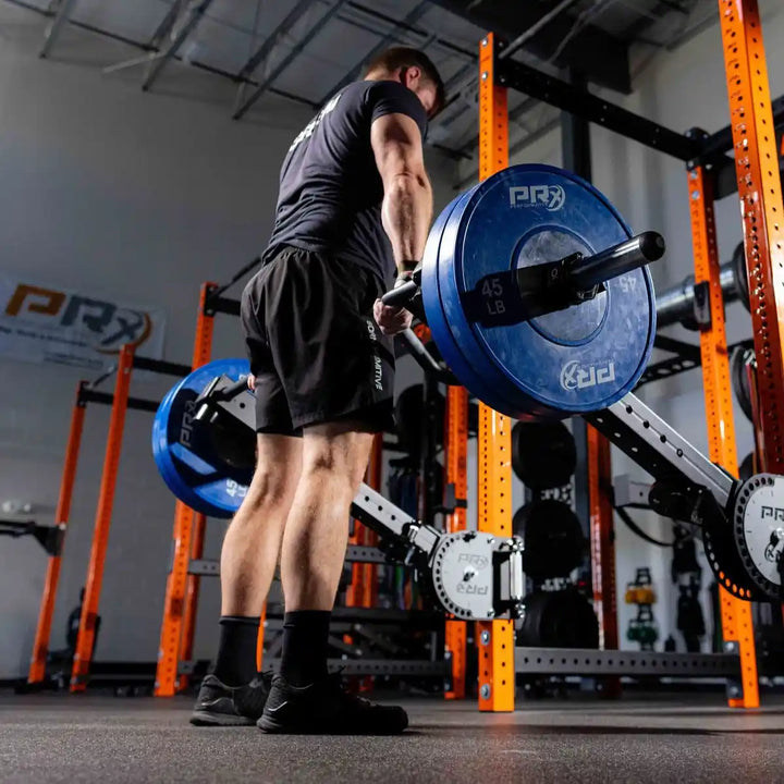 Person lifting a PRX performance barbell with blue PRX weight plates in a gym setting
