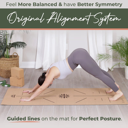 Woman in downward dog pose on a natural cork yoga mat with alignment guide lines printed across the surface, set in a bright room with potted plants and wooden props.