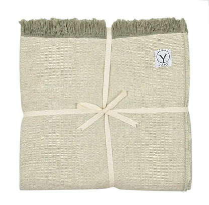 Folded organic cotton yoga blanket in cream and sage green with fringed edges and cream ribbon tie, Gayo brand label visible.