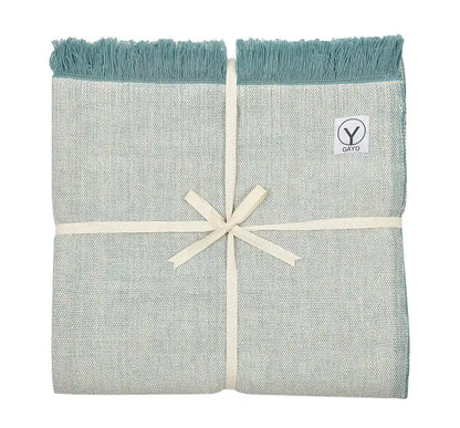 Organic cotton yoga blanket in light gray with teal fringe edges, tied with a cream ribbon and featuring a Gayo brand label.