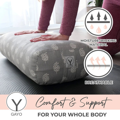 Person in burgundy socks pressing hands on a gray cylindrical yoga bolster with white floral pattern, showing moisture-wicking and breathable material features.