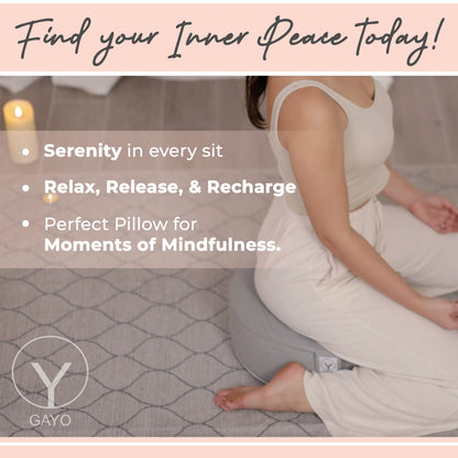 Woman in white clothing sitting in a meditative pose on a gray quilted buckwheat meditation cushion with a textured surface and brand logo visible.