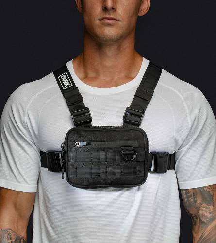 Man wearing a black tactical chest rig bag over a white shirt.