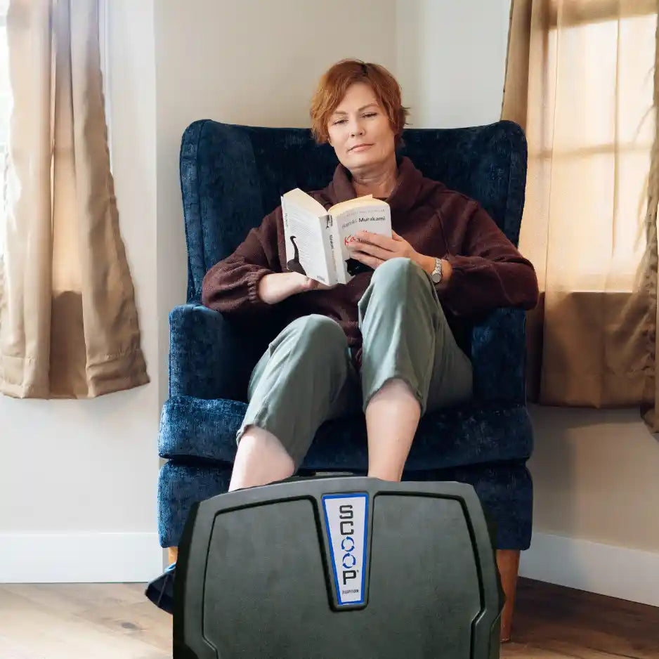 Person reading a book in a blue armchair while using the Helix Scoop Lateral Elliptical
