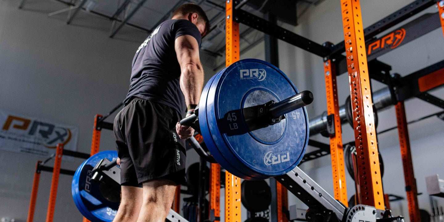 Gym worker performing barbell squat with loaded plates on rack.