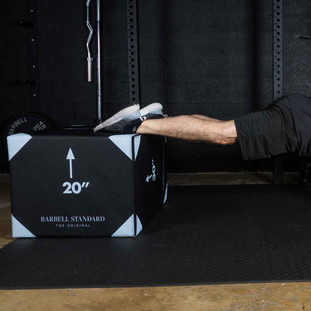 Person performing a decline push-up with feet on a 20-inch box in a gym.