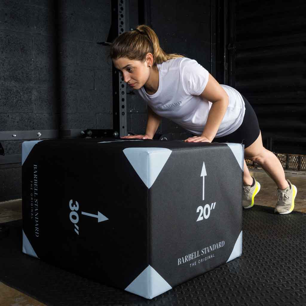 Woman performs incline push-up on a large gym jump box.
