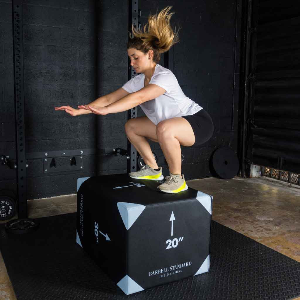 Athlete performing a box jump onto a 20-inch plyo box in gym.