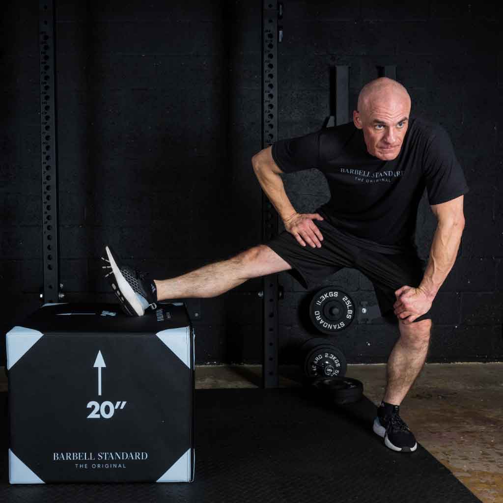 Athletic man in black stretches leg on a 20-inch jump box in the gym.