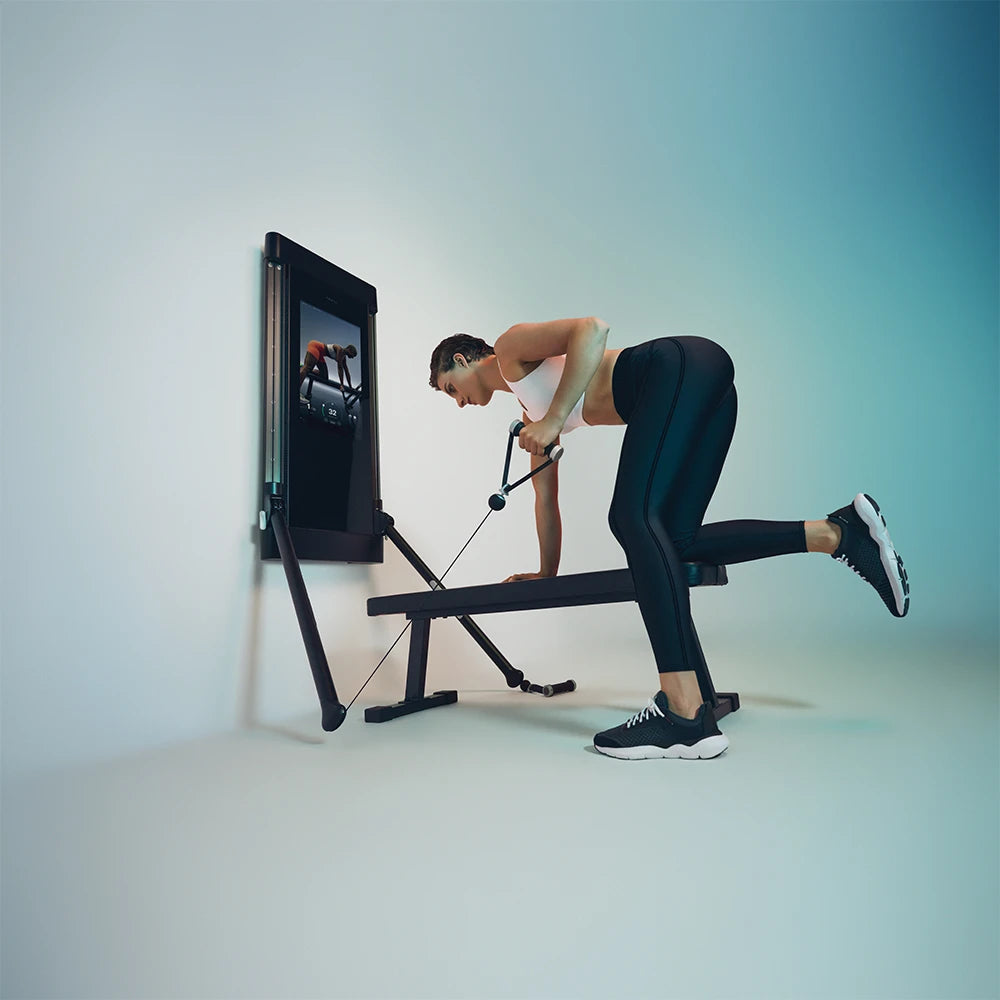 Person exercising using a Tonal 1 cable machine with a screen displaying workout videos on a light blue background