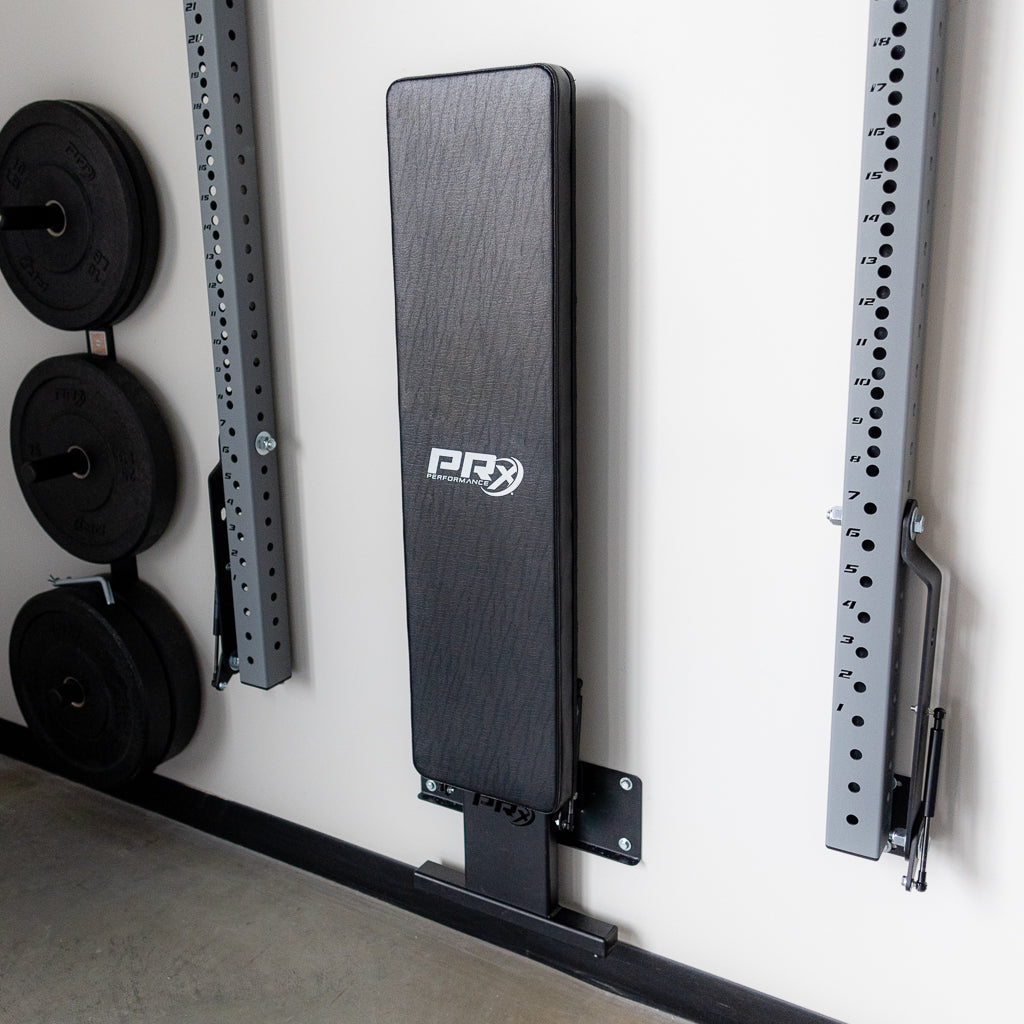 PRx flat folding bench mounted in gym with weight plates nearby