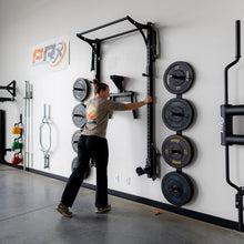 Woman in a gym adjusting a squat rack with weight plates on the wall.