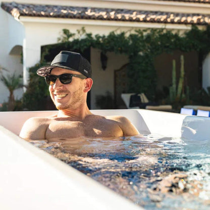 Man enjoying a relaxing soak in a modern hot tub, wearing sunglasses and a black cap with an American flag.