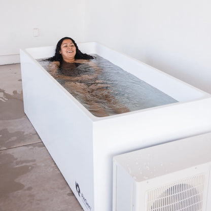 Woman enjoying a relaxing soak in a white ReGen cold plunge tub with water rippling around her.