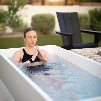 Woman relaxing in a modern white bathtub, enjoying a serene moment in a backyard setting.