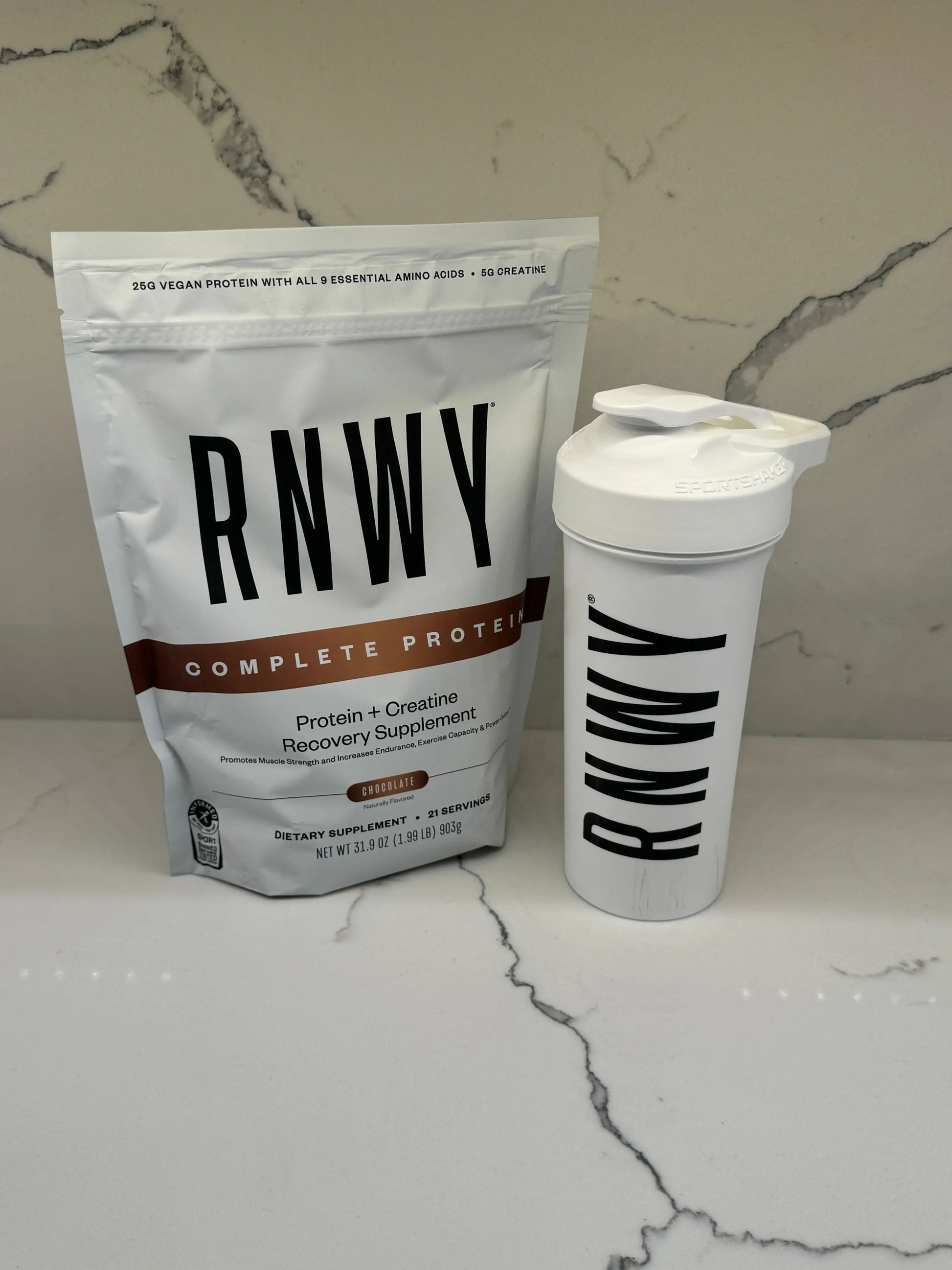 RNWY Complete Protein powder in white resealable pouch next to matching white shaker bottle with black logo, displayed on marble surface.