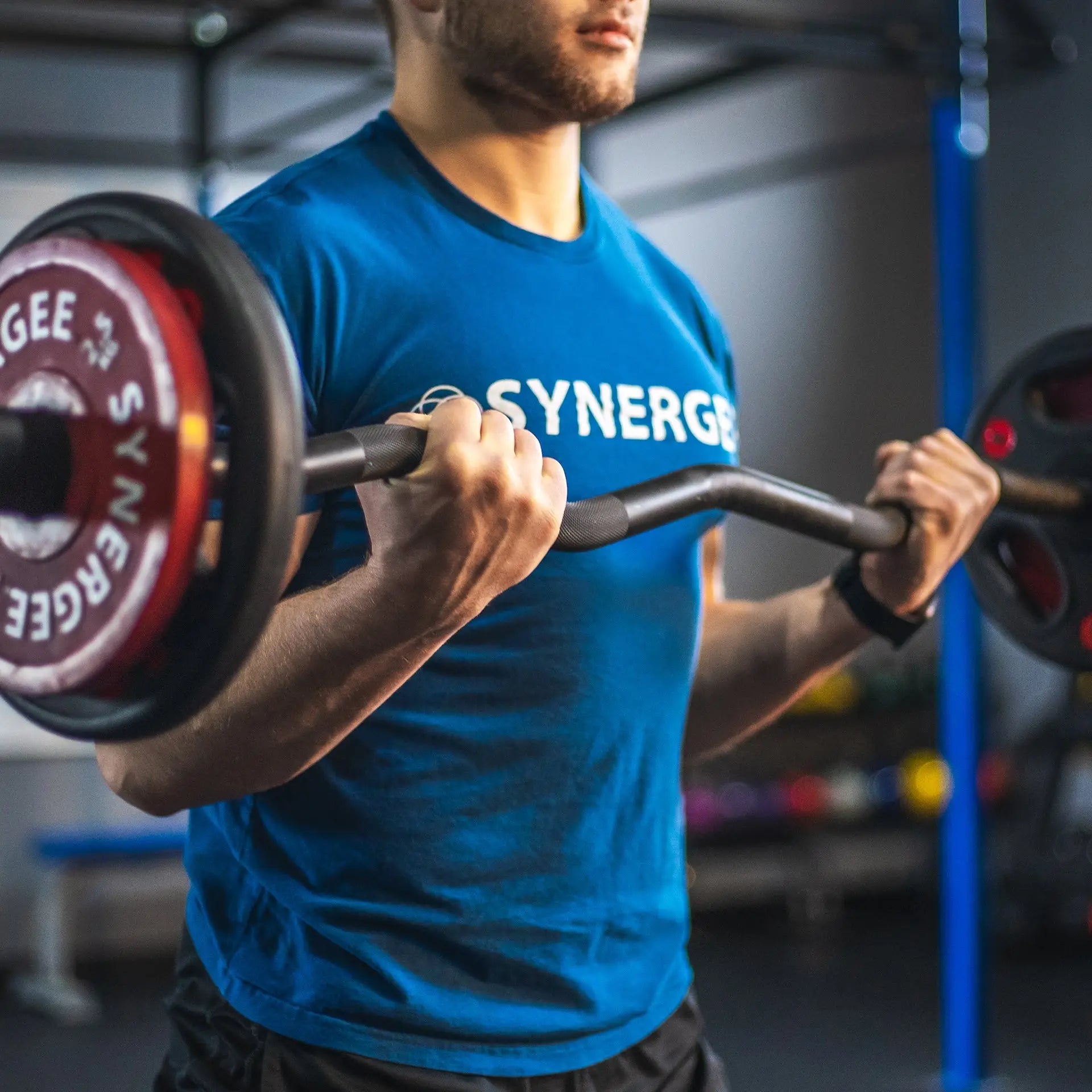 Man performing a bicep curl with a black curved barbell loaded with red weight plates in a gym setting.