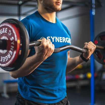 Man performing a bicep curl with a black curved barbell loaded with red weight plates in a gym setting.