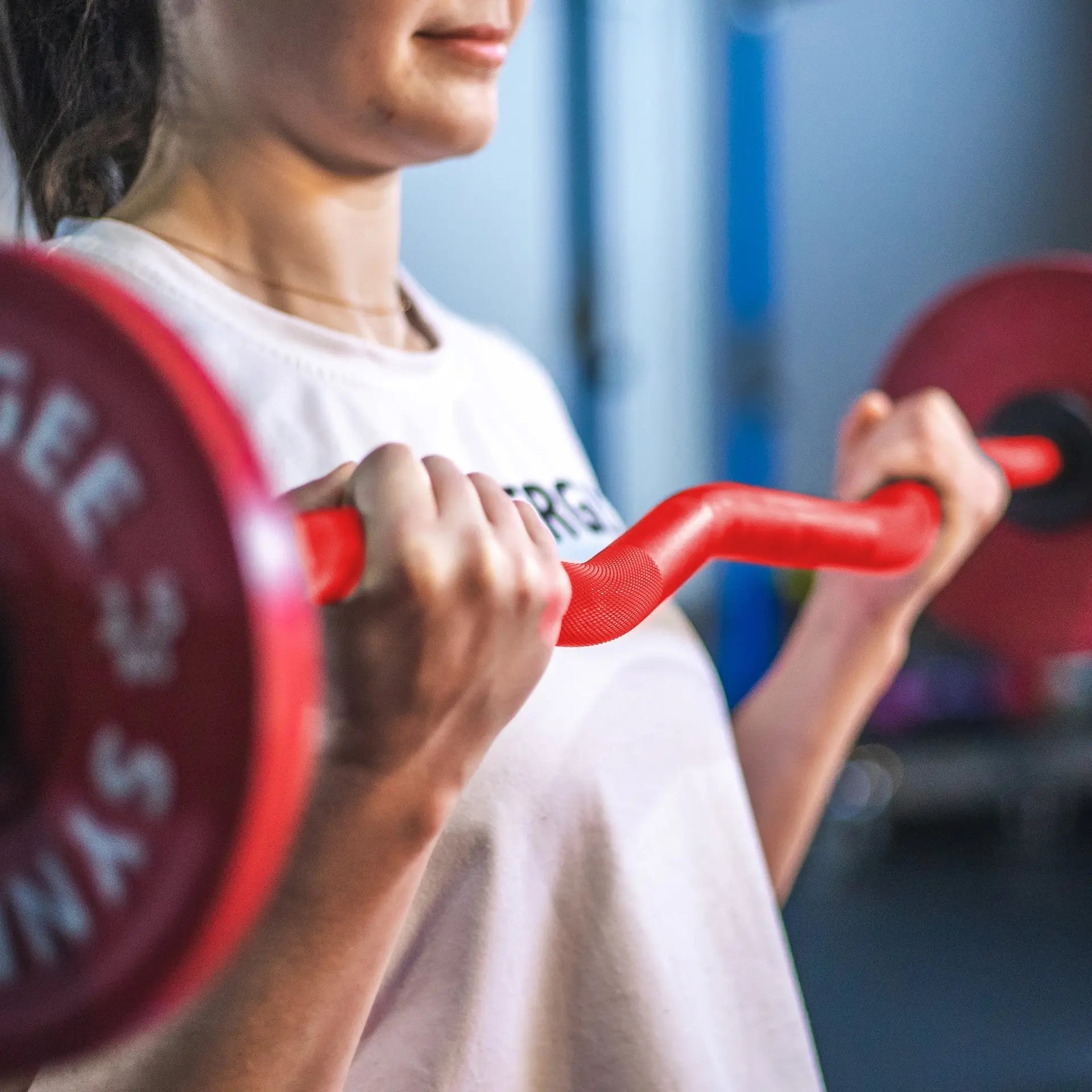 Woman holding red EZ curl bars with textured grip handles in a gym setting with blue backdrop.