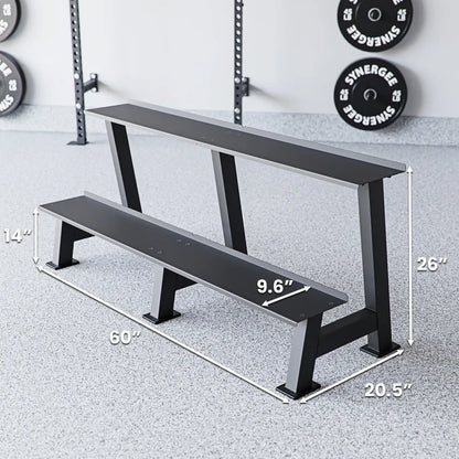 Two-tier black weight bench with metal legs positioned in a gym setting with a power rack and loaded plates visible in background. Dimensions labeled: 60" length, 26" height, 20.5" depth, and 9.6" seat width.