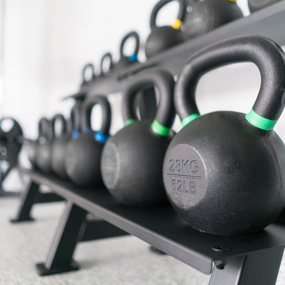 Row of black kettlebells with colored bands displayed on a gray storage rack, with the front kettlebell marked 28KG and 62LB.