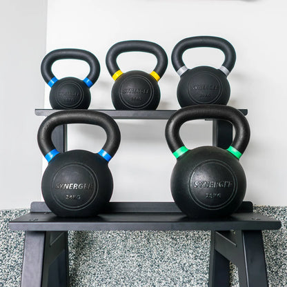 Five black cast-iron kettlebells with colored accent bands stored on a two-tier gray metal rack. Weight markings visible on each bell ranging from 10kg to 28kg.