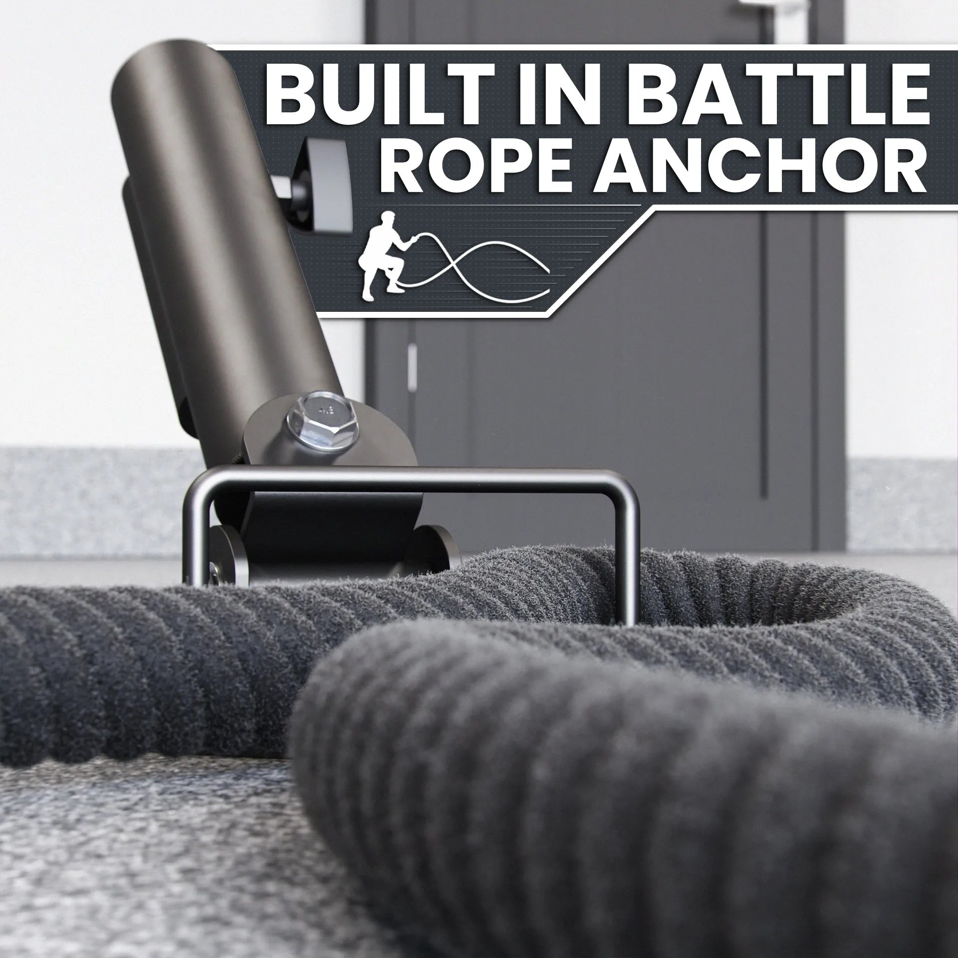 Black landmine platform with cylindrical steel sleeve and built-in battle rope anchor point, shown with gray battle rope coiled on gym floor.