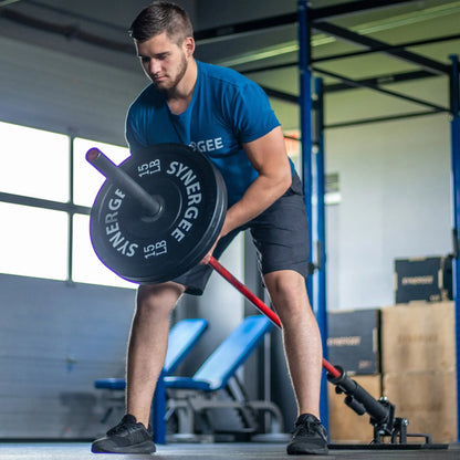 Man performing a landmine row exercise with a loaded barbell on a red landmine attachment in a gym setting.