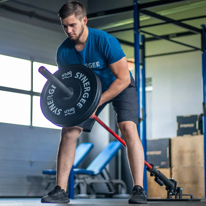 Man performing a landmine row exercise with a loaded barbell on a red landmine attachment in a gym setting.