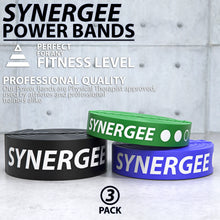 Three Synergee resistance power bands in black, green, and blue, coiled and displayed on a white concrete background.
