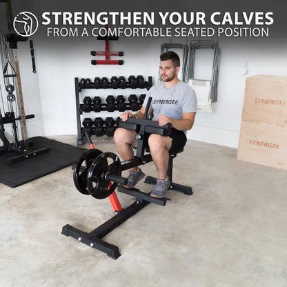 Man performing a seated calf raise on a black and red calf machine with weight plate loaded on the front, in a gym setting with dumbbells and equipment visible in the background.