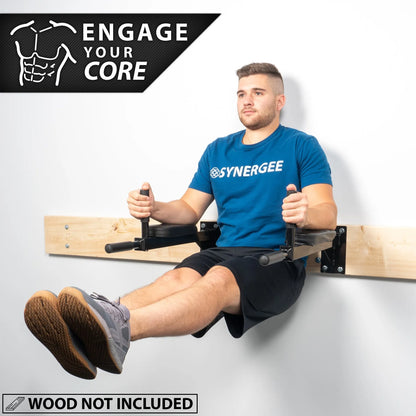 Man performing a core exercise on a wall-mounted dip station with black metal frame and handles, wearing a blue Synergee shirt and black shorts.