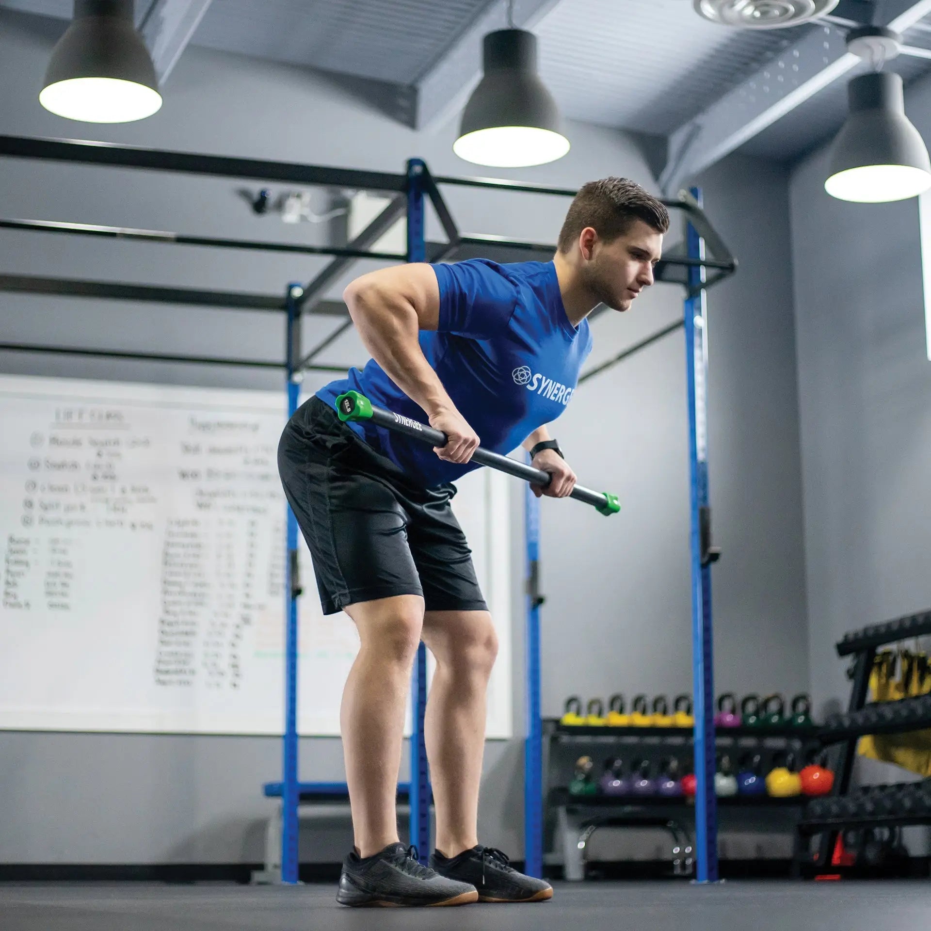 Man performing a weighted exercise with a black and green battle rope in a gym with blue rig frame and overhead lighting.