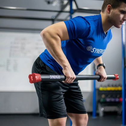 Man performing a bent-over row with a black Synergee weighted bar with red end caps in a gym setting.
