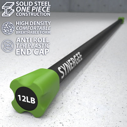 Black steel weighted bar with green foam end cap labeled 12LB, resting on speckled gray floor. The bar features solid steel construction with high-density breathable foam padding and anti-roll TPR plastic end cap.