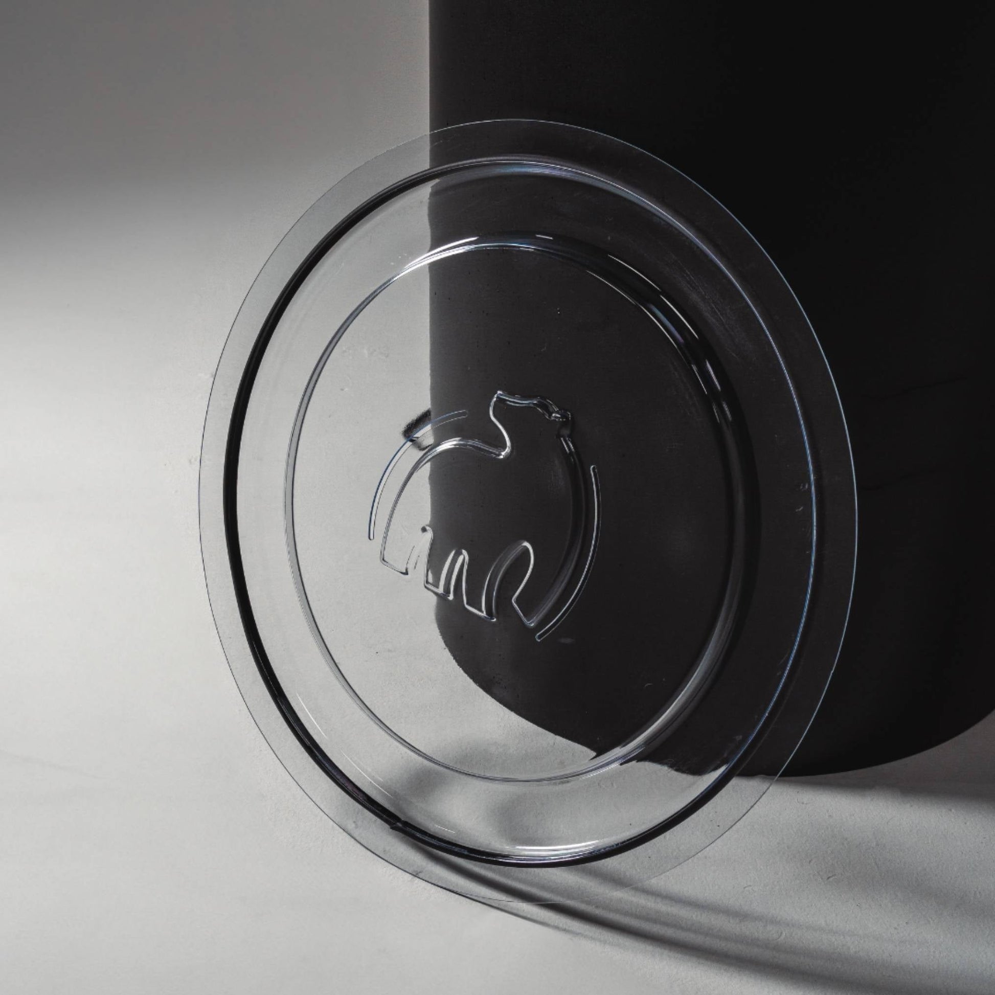 A clear plastic lid with a polar bear logo resting beside a black container on a light surface.