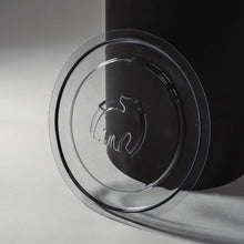 A clear plastic lid with a polar bear logo resting beside a black container on a light surface.