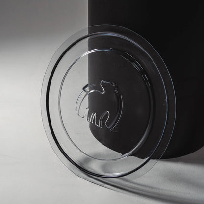 A clear plastic lid with a polar bear logo resting beside a black container on a light surface.