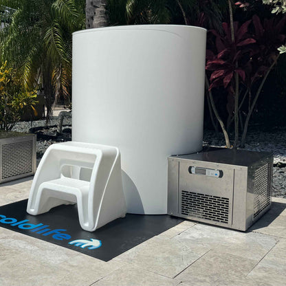 A white cylindrical unit next to a metallic cooling unit, with a small white step stool in front, all set on a black mat with the text coldlife visible, surrounded by tropical plants.