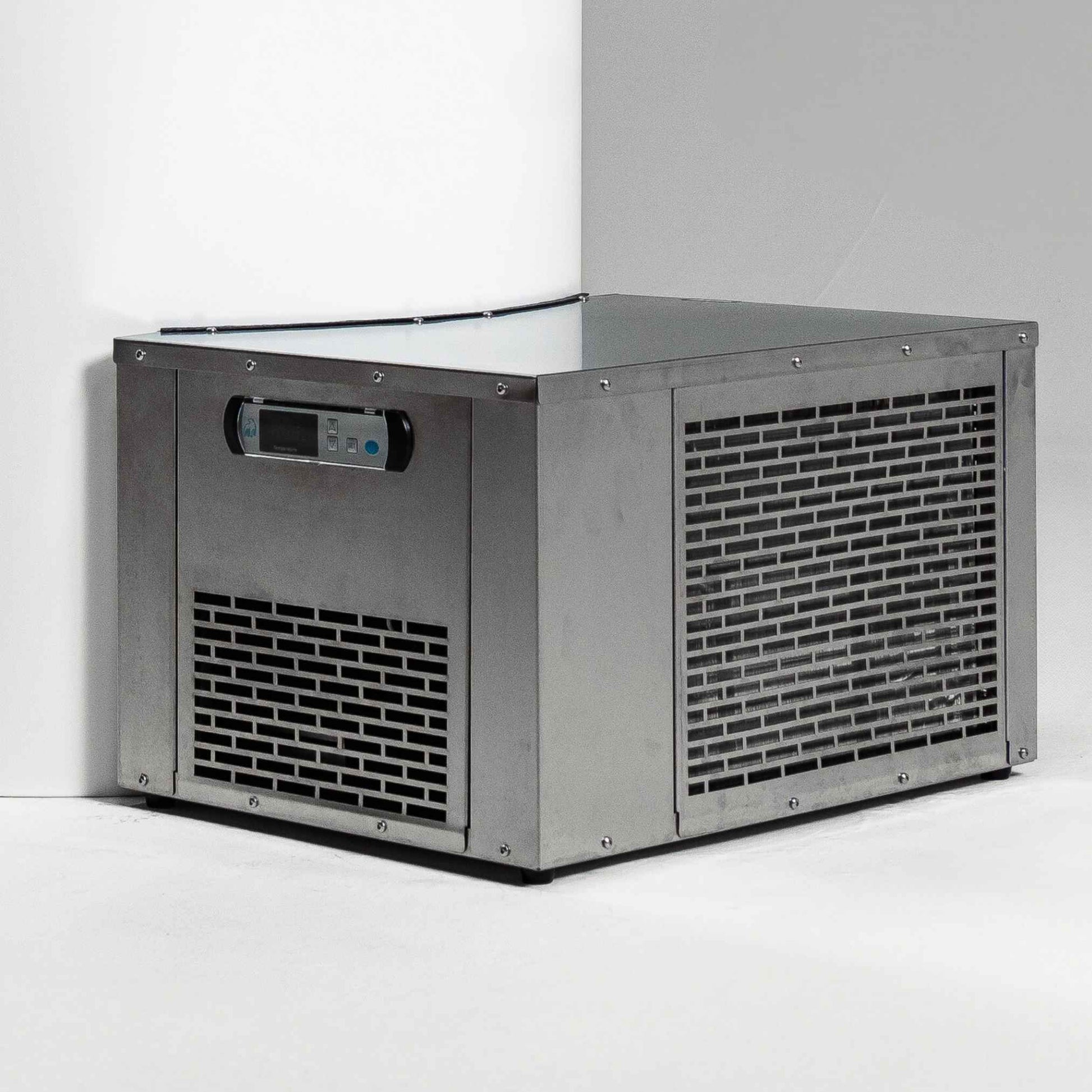 A metal ice maker machine with a digital control panel, positioned in a corner against a white wall.
